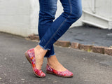 A person wearing blue jeans and red ballet flats with a multicolored design on the shoe's surface. Comfortable European women's shoes.