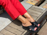 A person wearing Via Nova Bloo sandals in black color, with enough space to insert a foot , v throat with crossover straps and wedge heel. Comfortable footbed.
